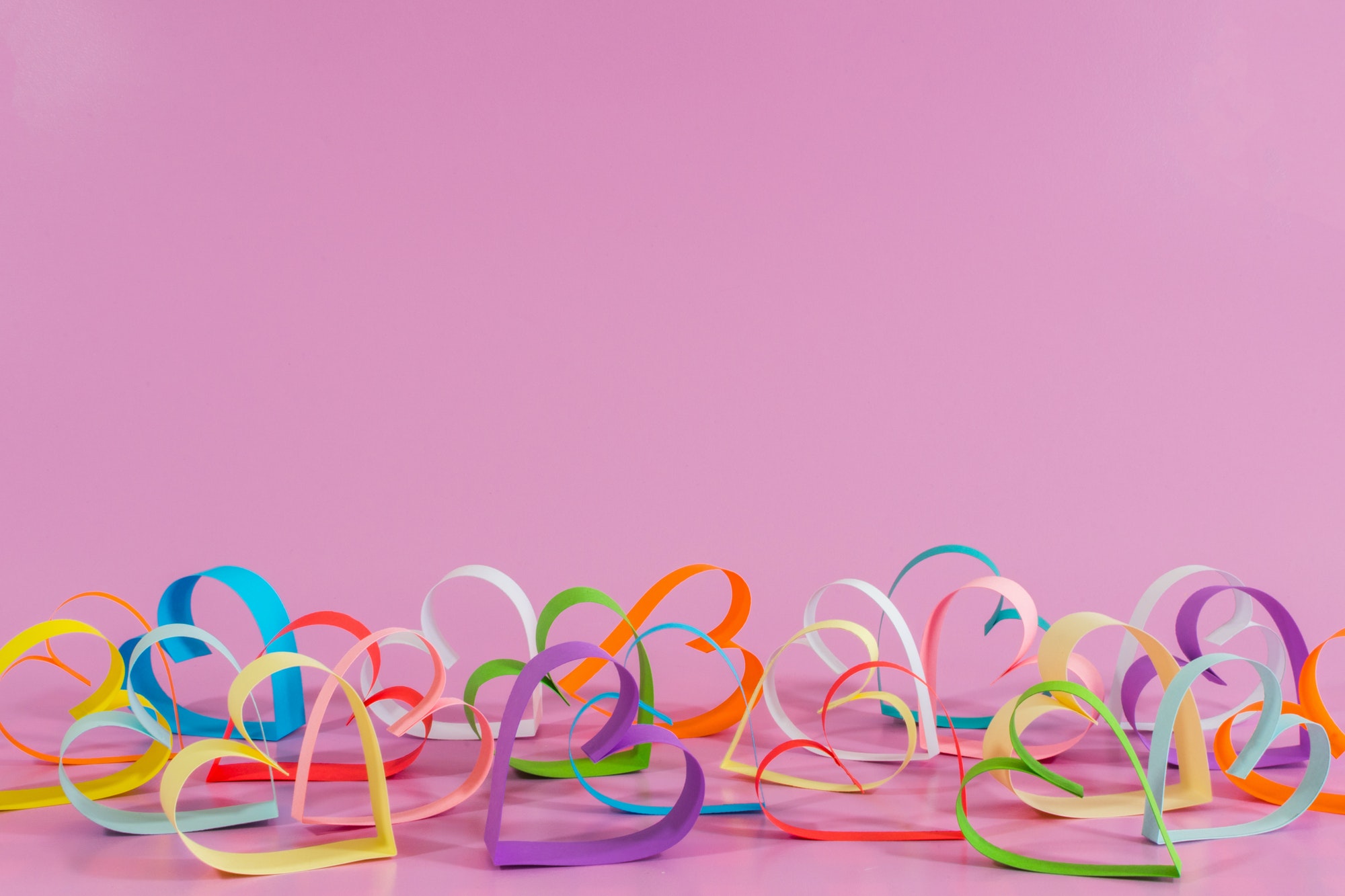 Closeup shot of colorful love hearts from paper isolated on pink background