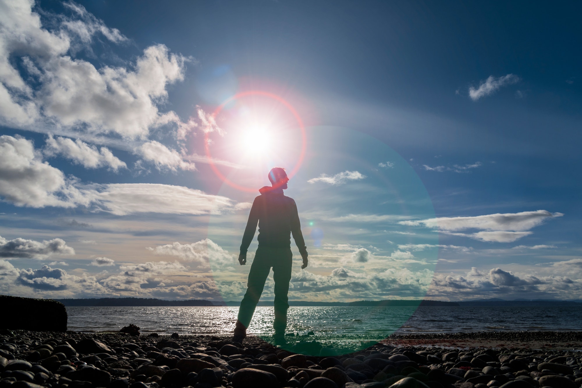 Silhouetted man standing by the sea in lens flare aura